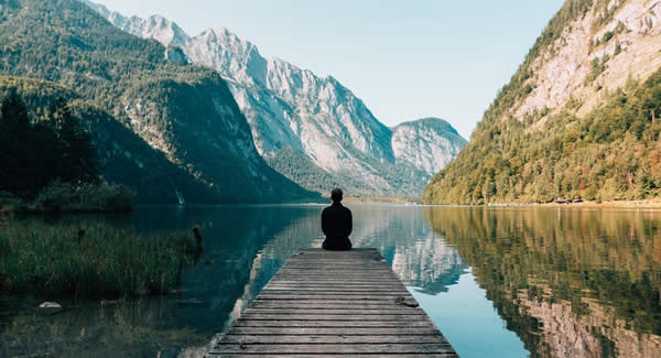 person sitting at the end of a dock on a lake in the mountains 