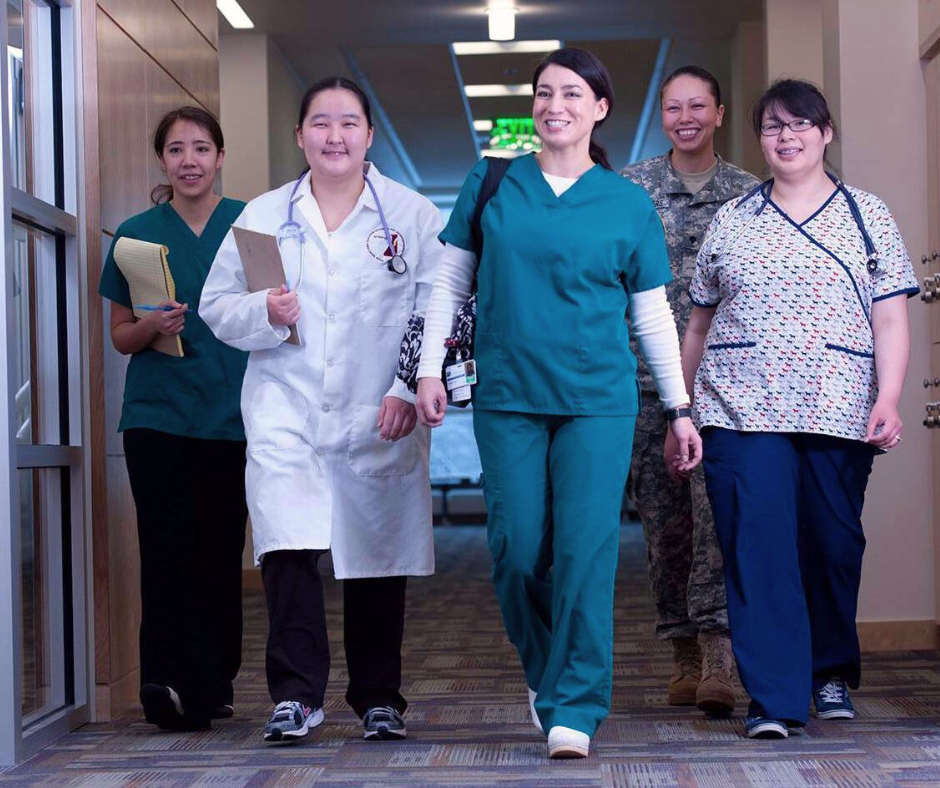 four medical students in scrubs walk along a corridor