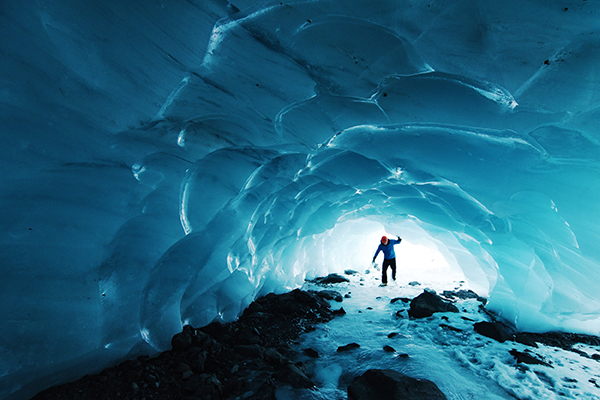 A person walks through a blue ice tunnel